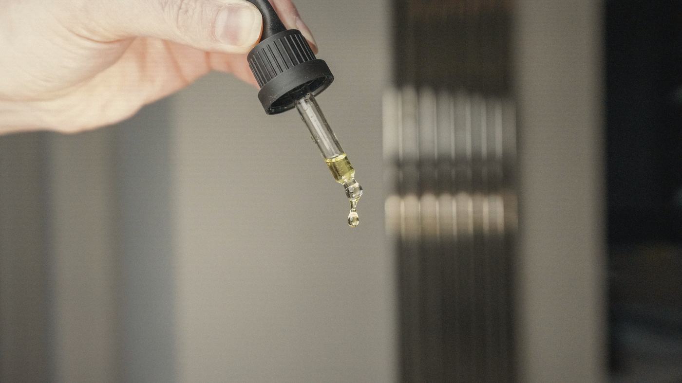 A glass dropper, a single drop of oil forming at its tip